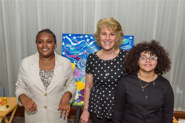 Two students and an artist smile at the camera with their abstract painting behind them.